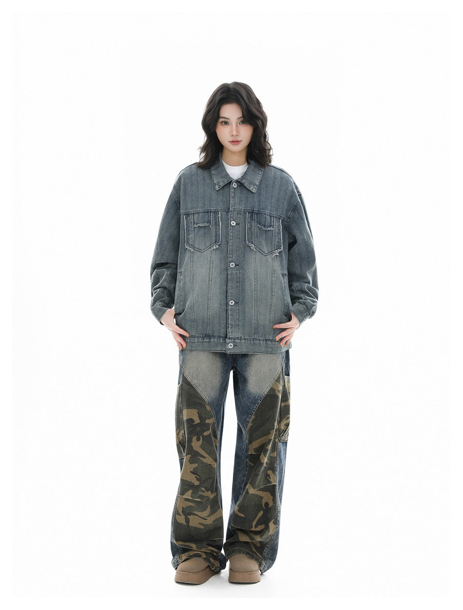 Model wearing an oversized faded blue-gray denim jacket with chest pockets and loose jeans with camouflage panels.