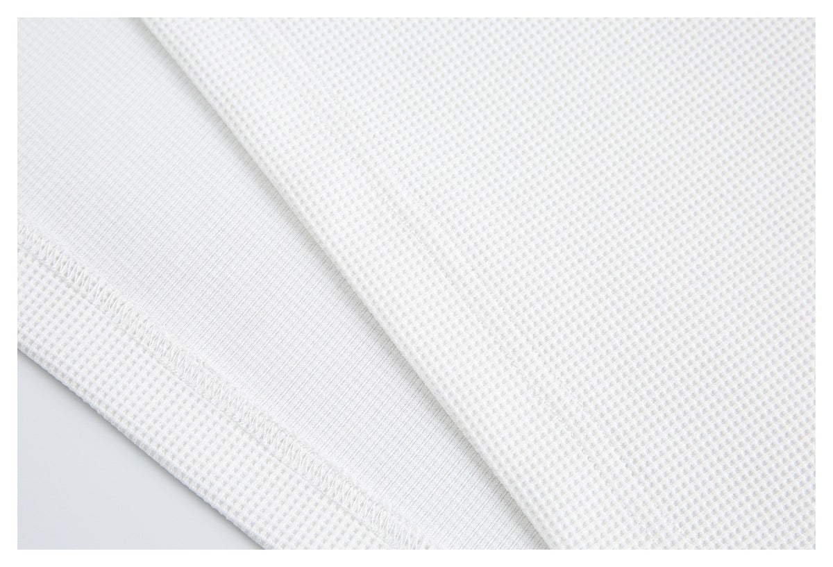 Close-up of white waffle-knit fabric folded to show a smooth inner layer and stitched edge.