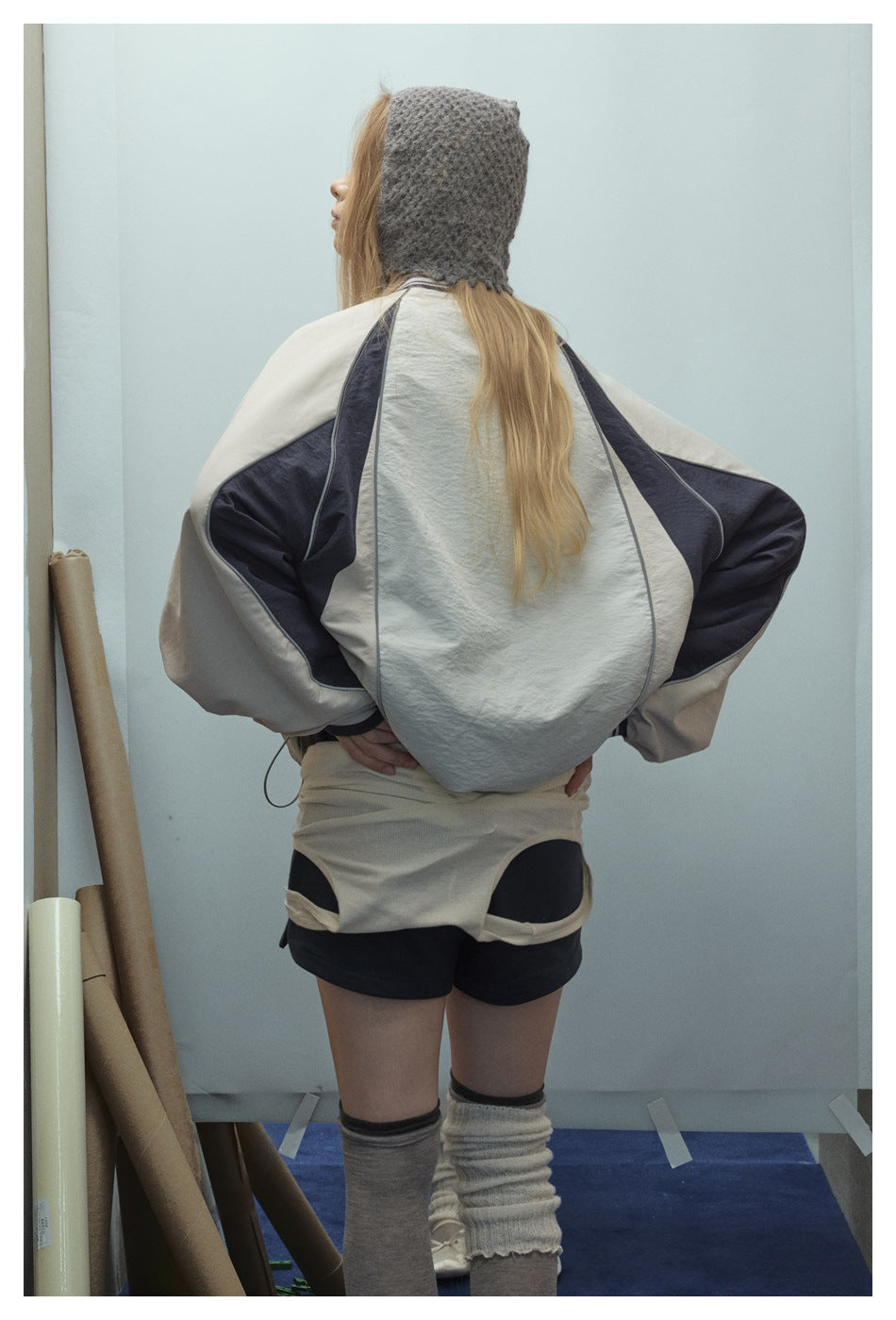 Rear view of a model wearing an oversized cream sweatshirt with dark sleeve panels and contrast piping.