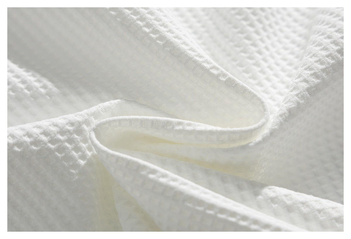 Close-up of white textured fabric draped in overlapping folds, showing its raised weave and bound edge.