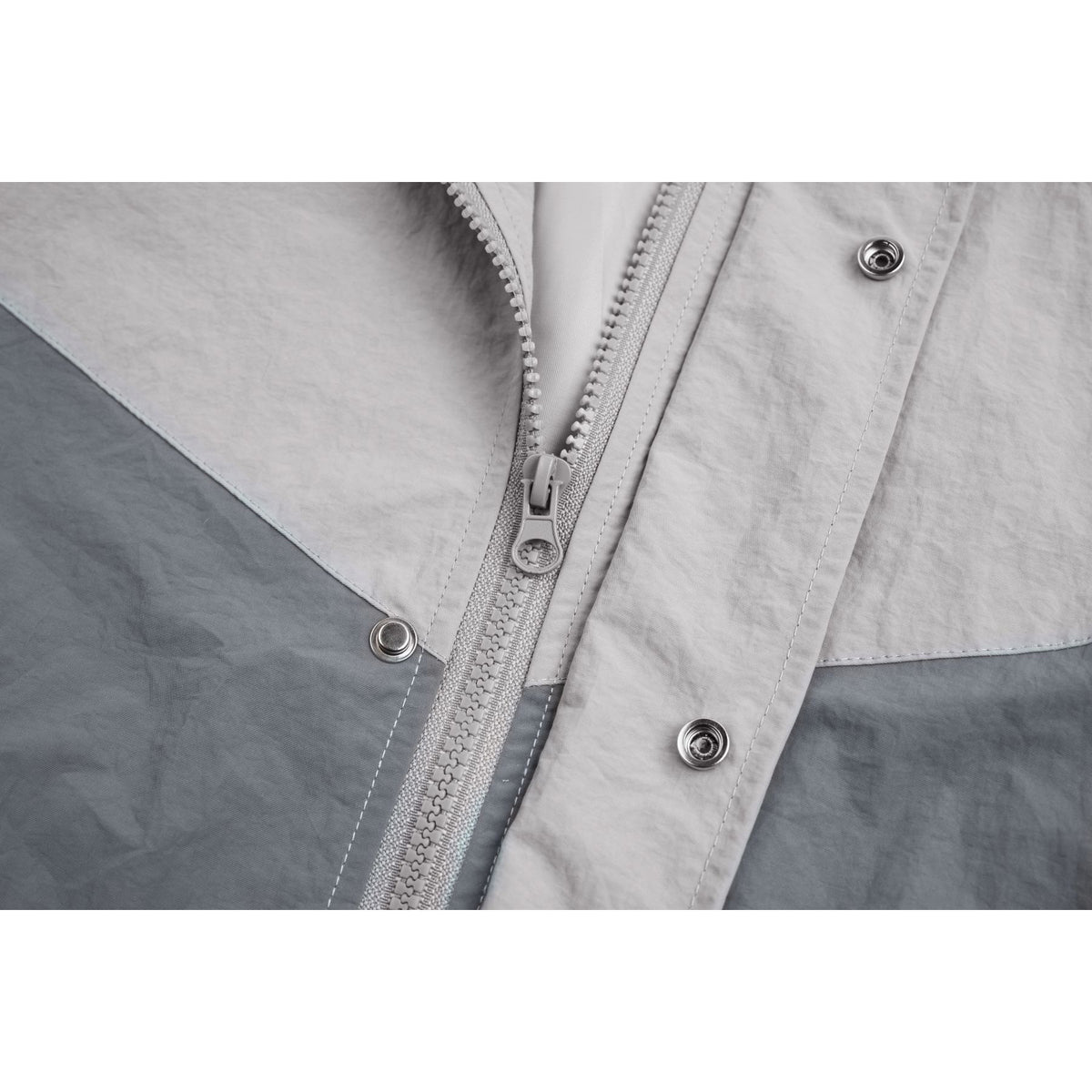 Close-up of the jacket's light gray zipper, snap-button storm flap, and contrasting gray-blue panels.