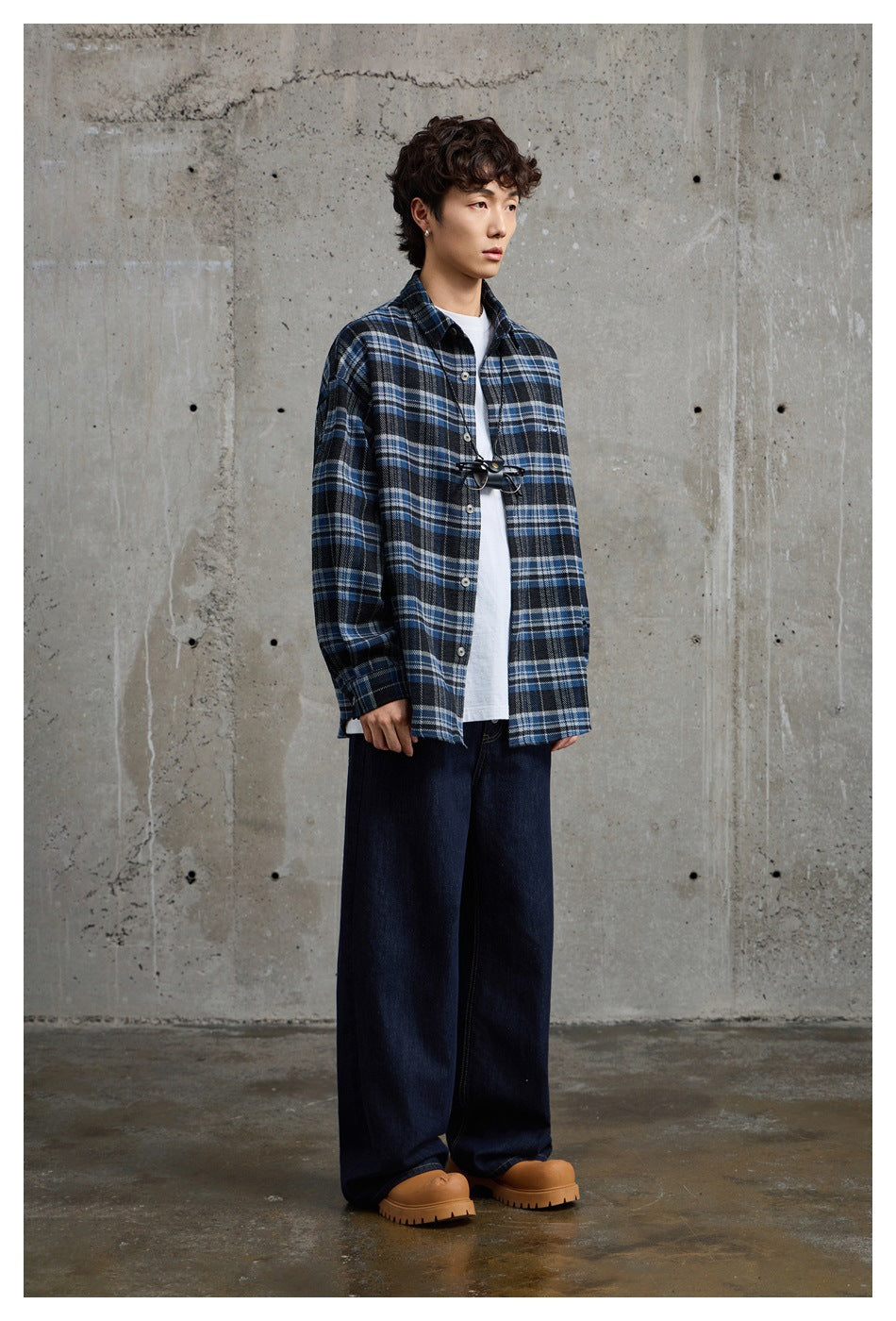 Model wearing open blue plaid shirt over a white tee with wide dark jeans and tan chunky boots