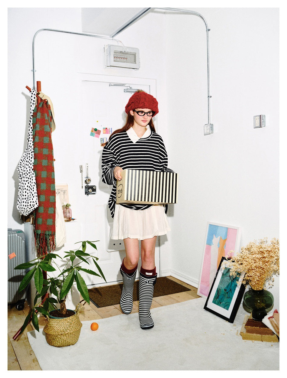 Model in black and white striped loose top with white skirt, red beret and striped boots, carrying a striped box