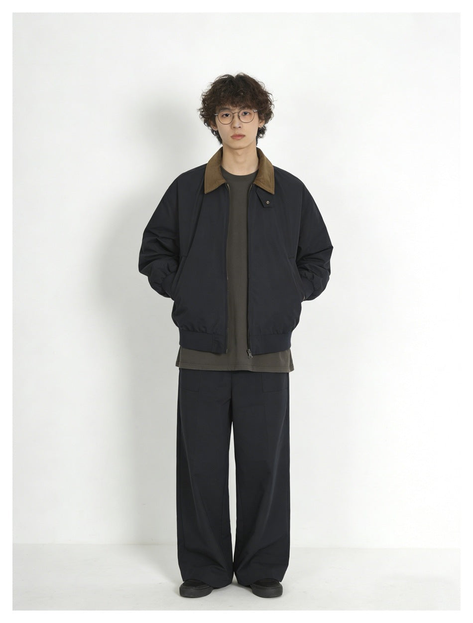 Full-length front view of a model wearing a navy jacket with brown collar, dark shirt, and wide-leg trousers.