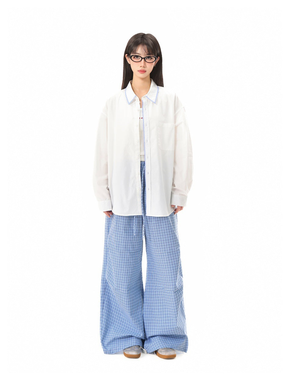 Model wearing an open white button-up shirt with blue striped trim over a tank top and blue plaid wide-leg pants