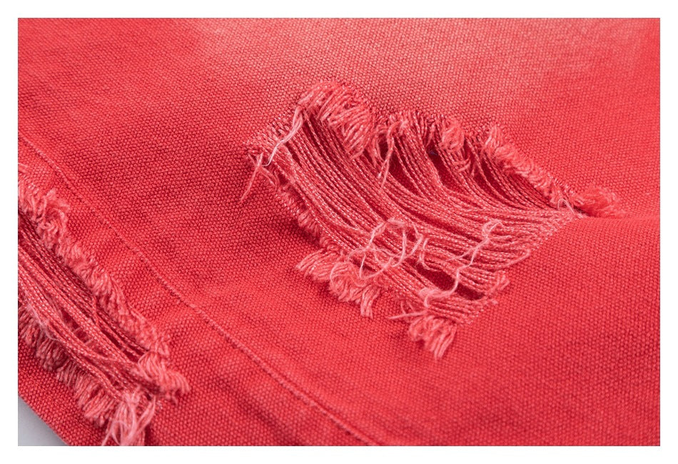 Close-up of coral-red fabric with a large frayed, distressed slit and loose threads.