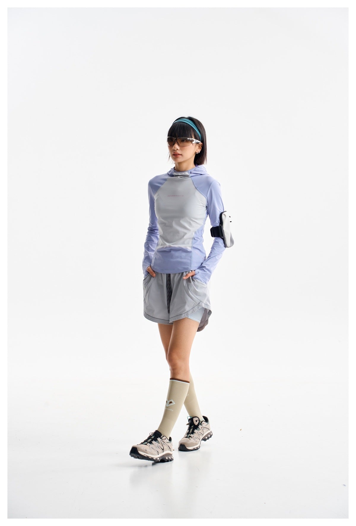 Model in a light blue and pale gray hooded top and gray shorts, posing in a three-quarter view.