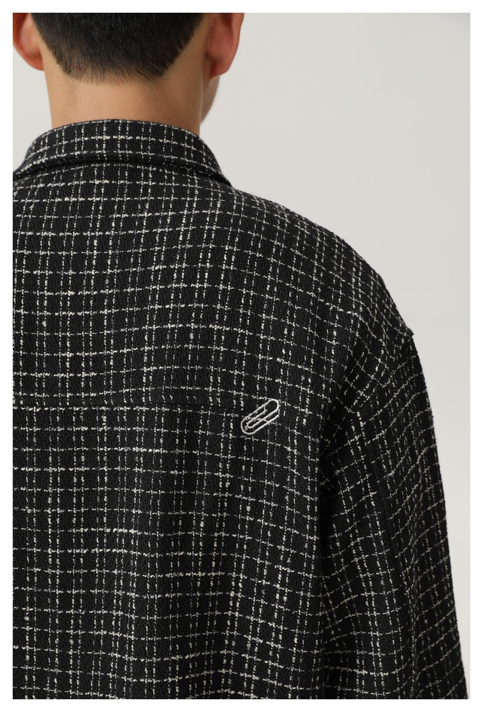 Close-up rear view of a model wearing a black-and-white plaid shirt jacket with a small embroidered emblem.