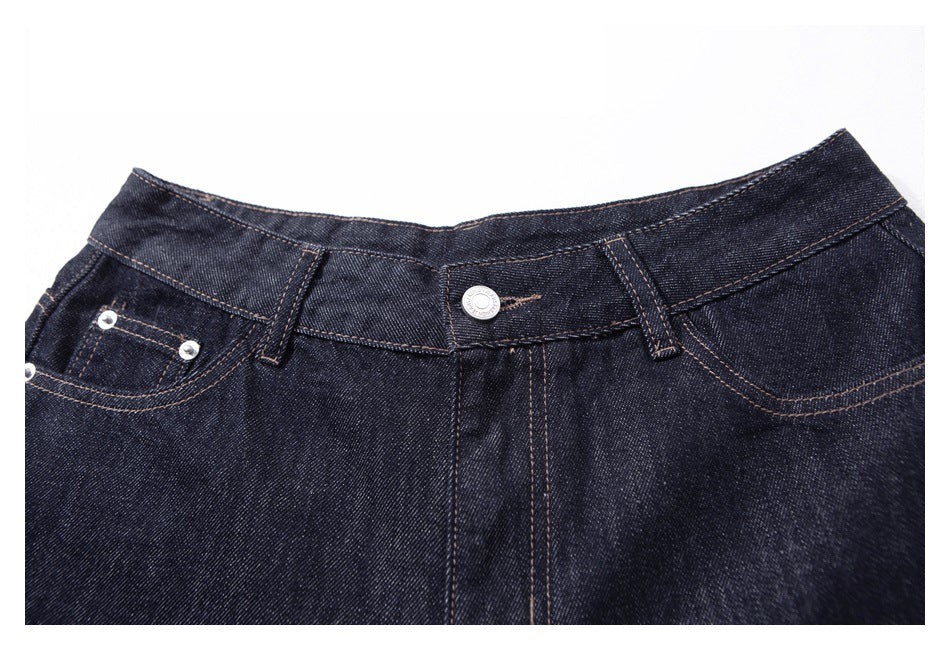 Close-up of dark indigo jeans showing the front button, waistband, belt loops, and riveted pockets.