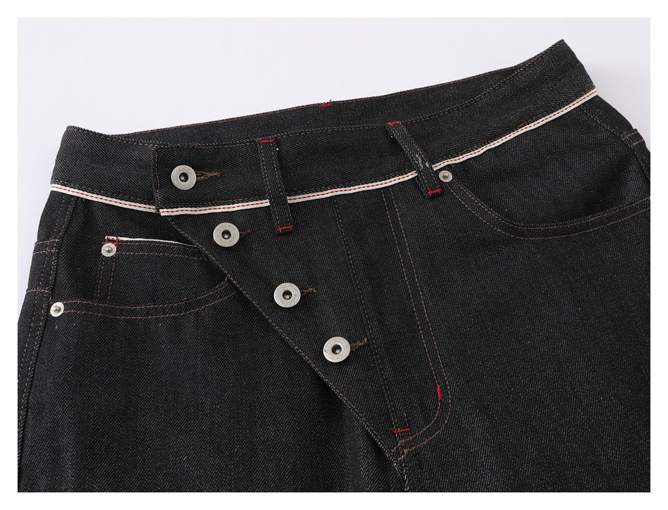 Close-up of black jeans with an open button fly, curved pockets, contrast stitching and white-and-red waistband trim.