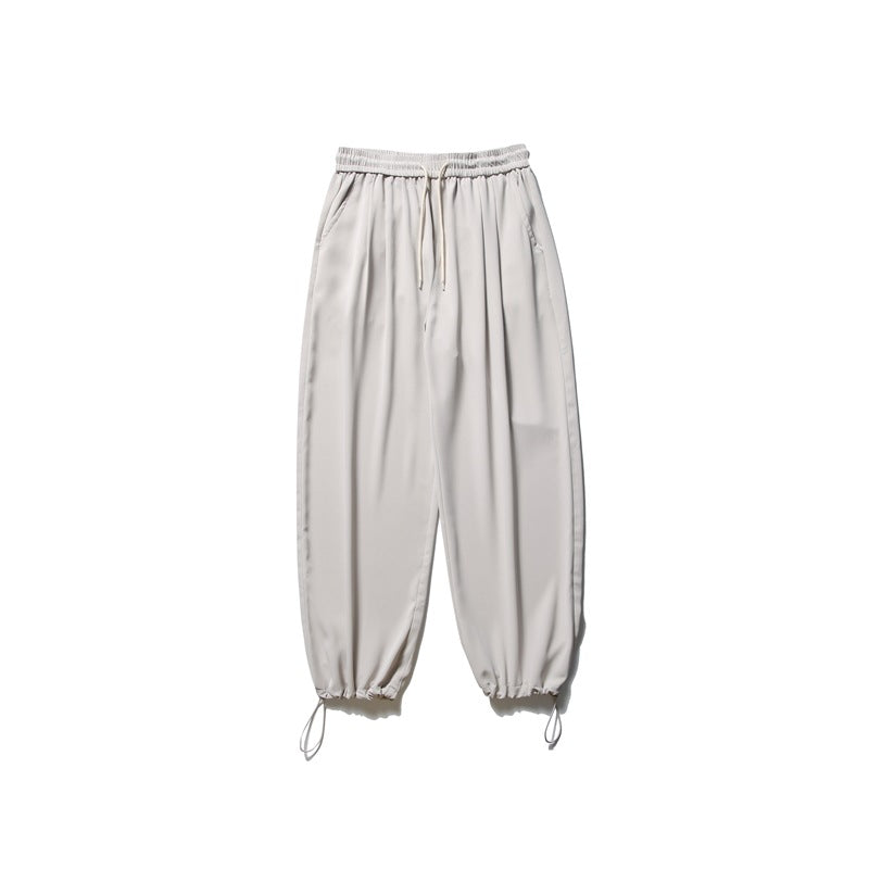 Light gray jogger pants with a drawstring elastic waist, angled pockets, and gathered cuffs with dangling cords.