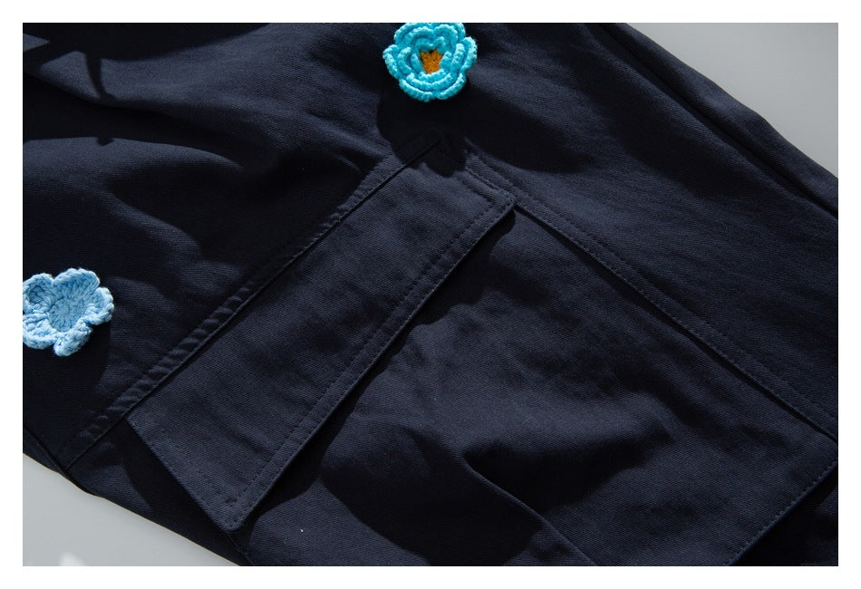Close-up of dark navy bottoms with patch pockets and small blue crocheted flower details.