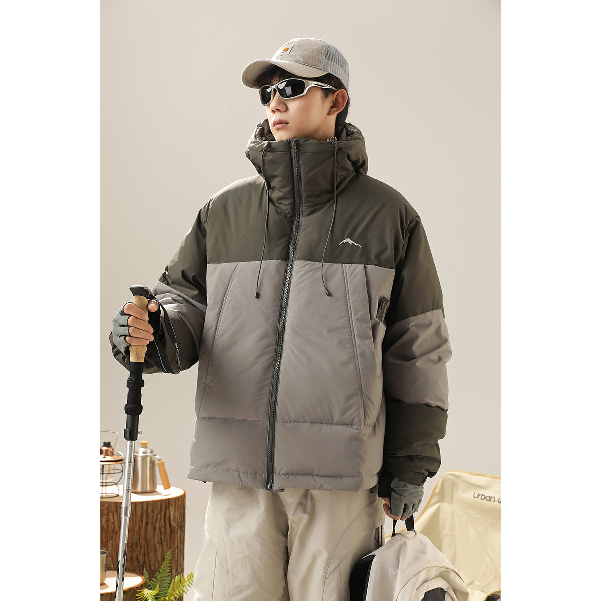 Model wearing an olive-and-gray color-block hooded jacket with a front zipper and high collar.