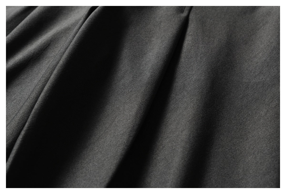 Close-up of dark charcoal fabric draped in soft folds, showing its fine diagonal weave.