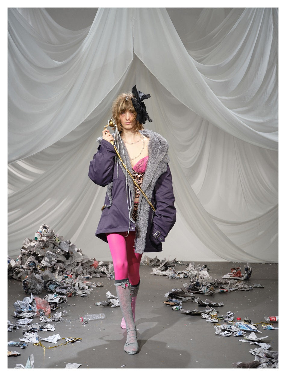 Model walking in a deep plum parka with gray textured trim, styled with vivid pink leggings and a leopard-print outfit.