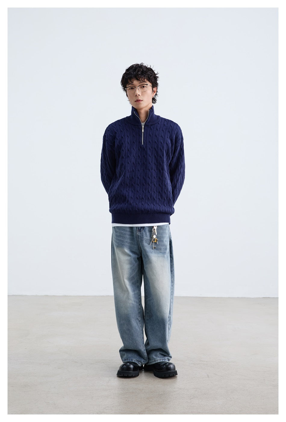 Full-length front view of a model wearing a navy cable-knit quarter-zip sweater and loose light-wash jeans.
