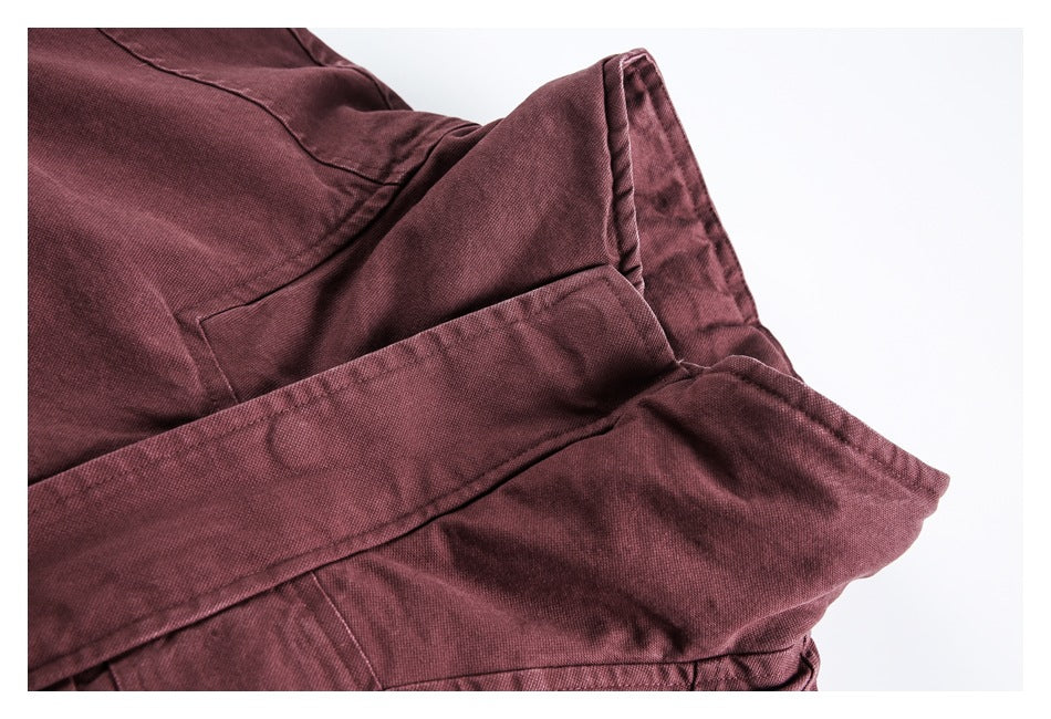 Close-up of burgundy garment fabric with layered stitched panels and a wide folded edge.