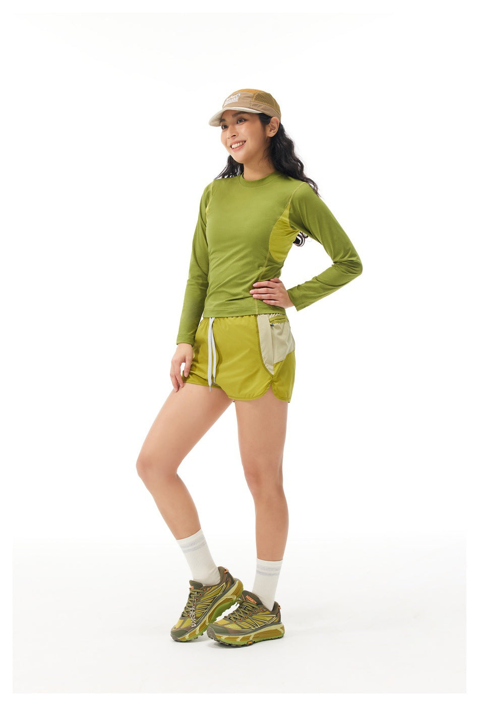 Three-quarter view of a model wearing an olive-green long-sleeve top and yellow-green shorts with contrasting side panels.