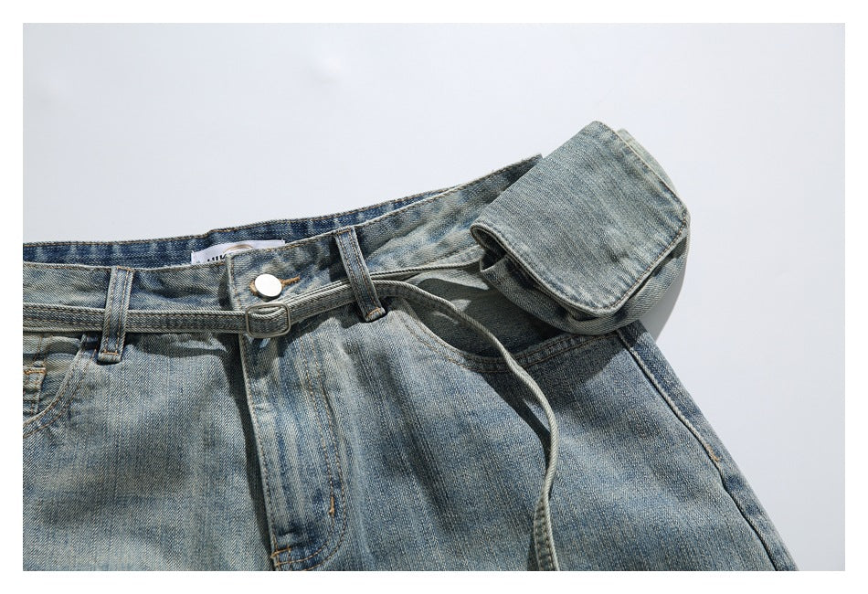 Close-up of the jeans' buttoned waistband, slim belt, belt loops, and attached denim pouch.