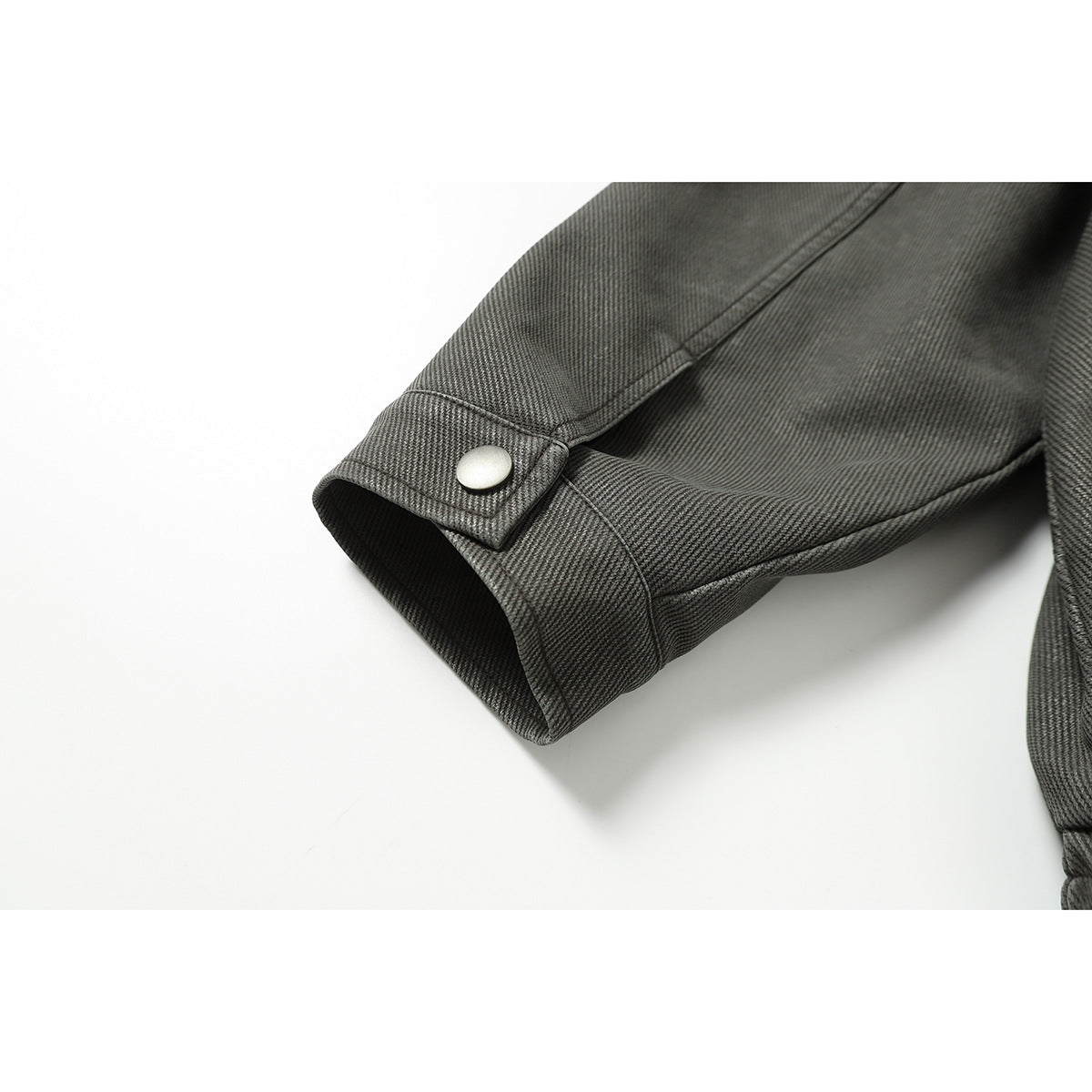 Close-up of a charcoal gray jacket sleeve cuff with an adjustable metal snap tab.