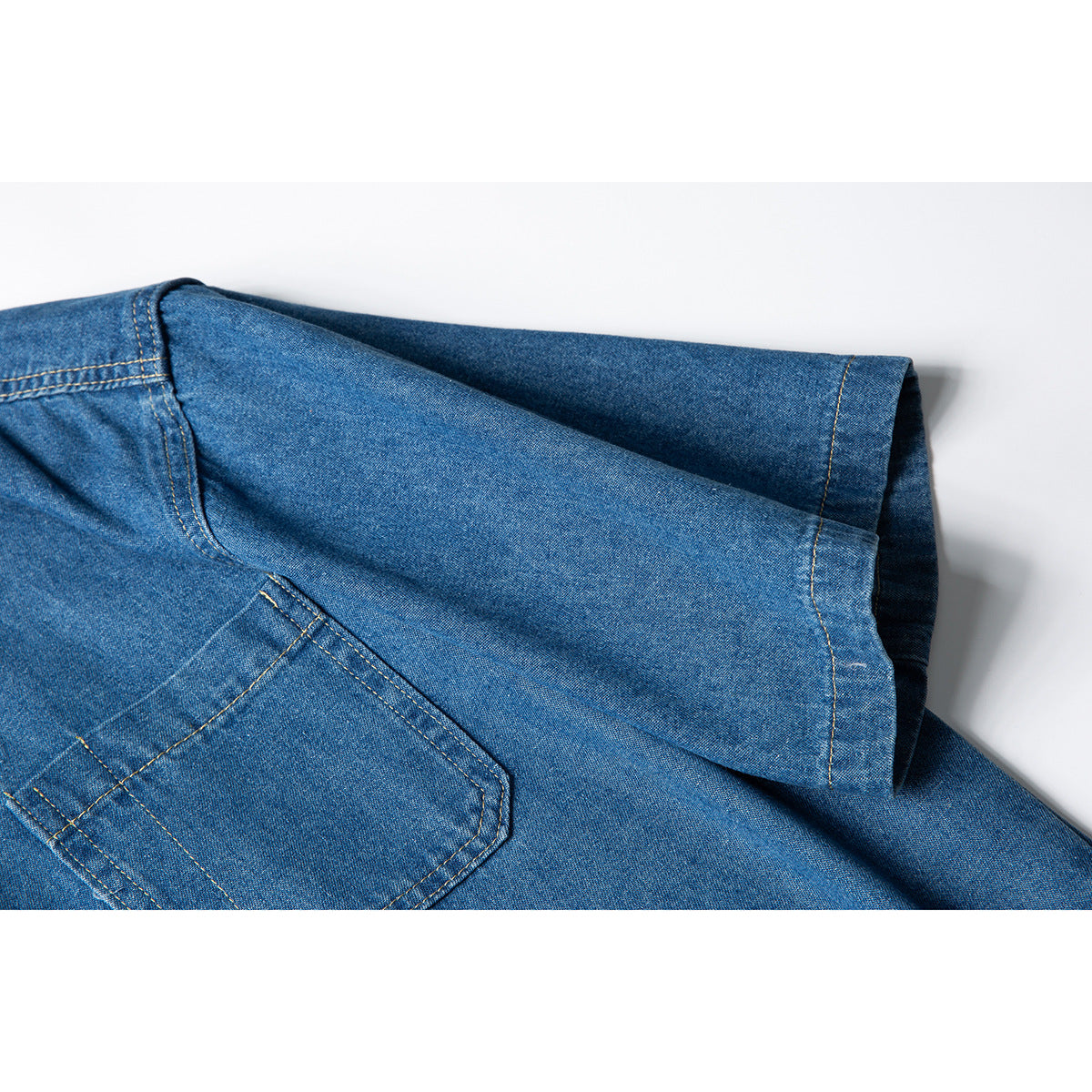 Close-up of a blue denim shirt sleeve and chest pocket, showing contrast stitching.