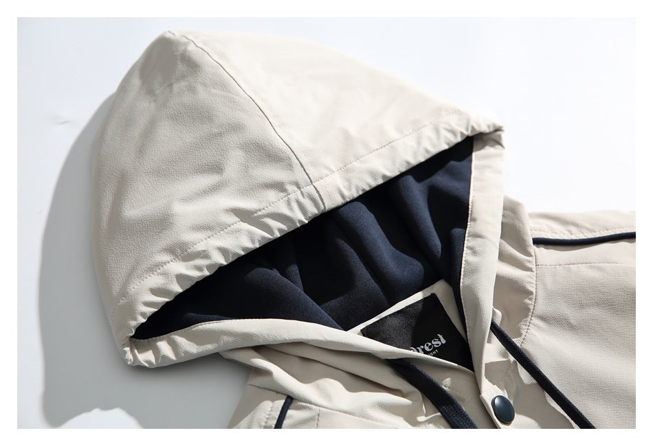 Close-up of an off-white jacket hood showing its dark lining, drawcord, piping and snap fastener.