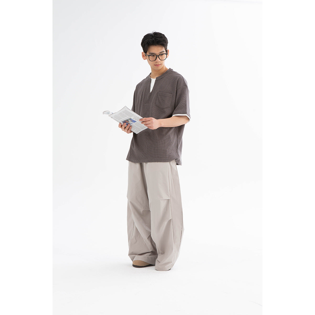 Model wearing a charcoal-gray short-sleeve split-neck shirt with white trim and chest pocket, with light wide-leg pants.