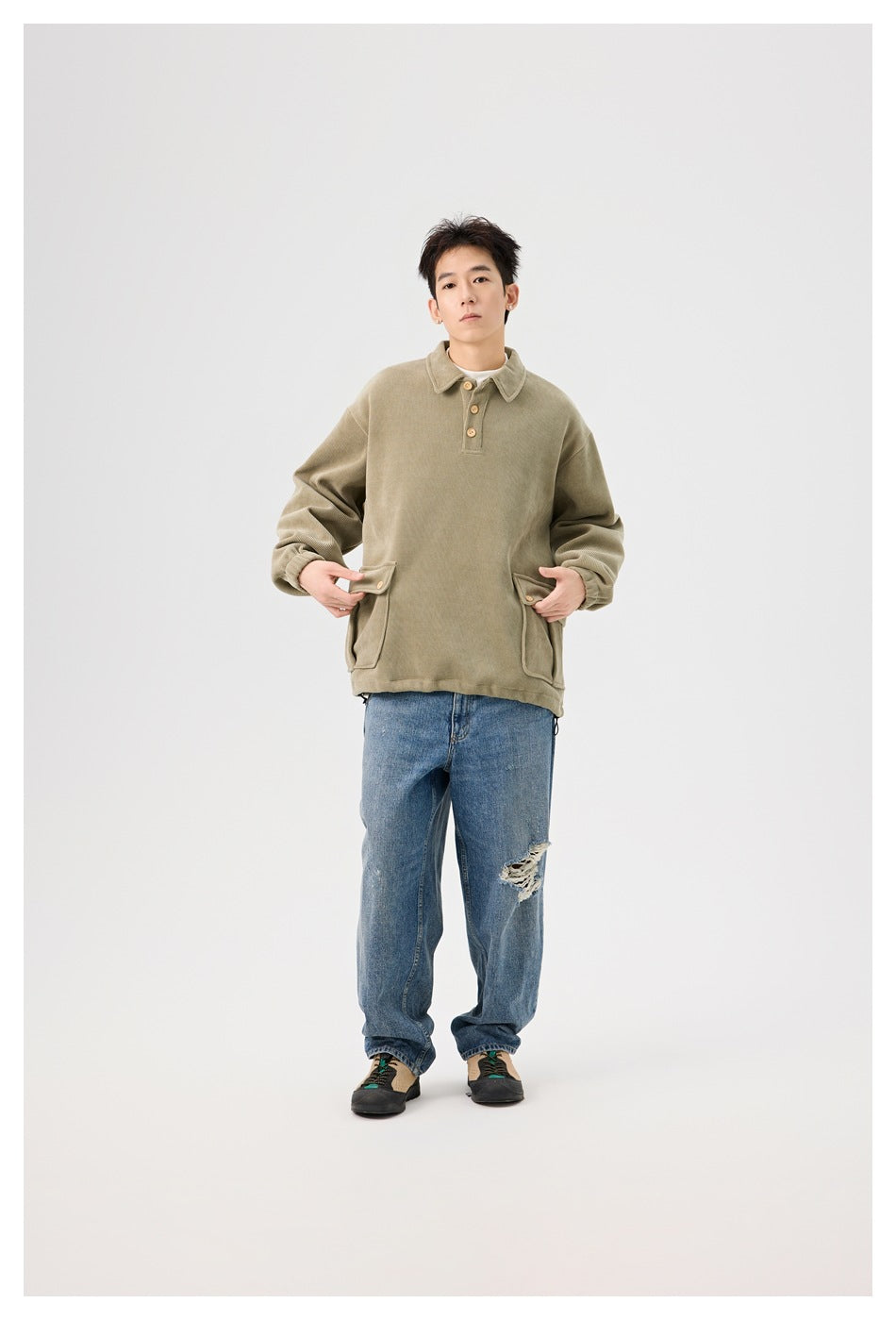 Model wearing the olive pullover with polo collar and flap pockets over a white tee, with distressed blue jeans