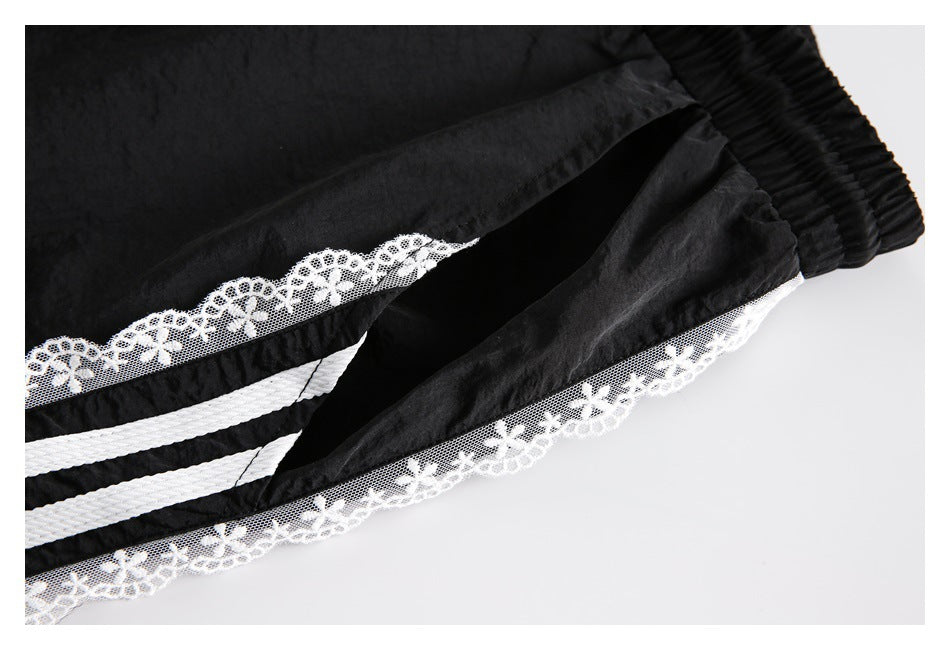 Close-up of black pants showing a folded opening bordered with white stripes and floral lace.