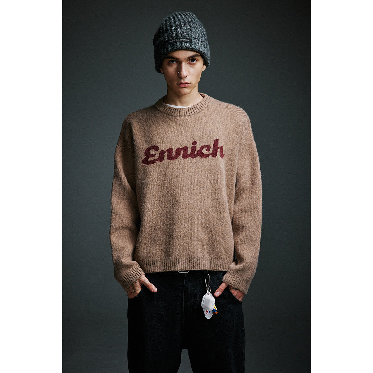 Front view of a model in a tan crewneck sweater with burgundy script lettering and a dark ribbed beanie.