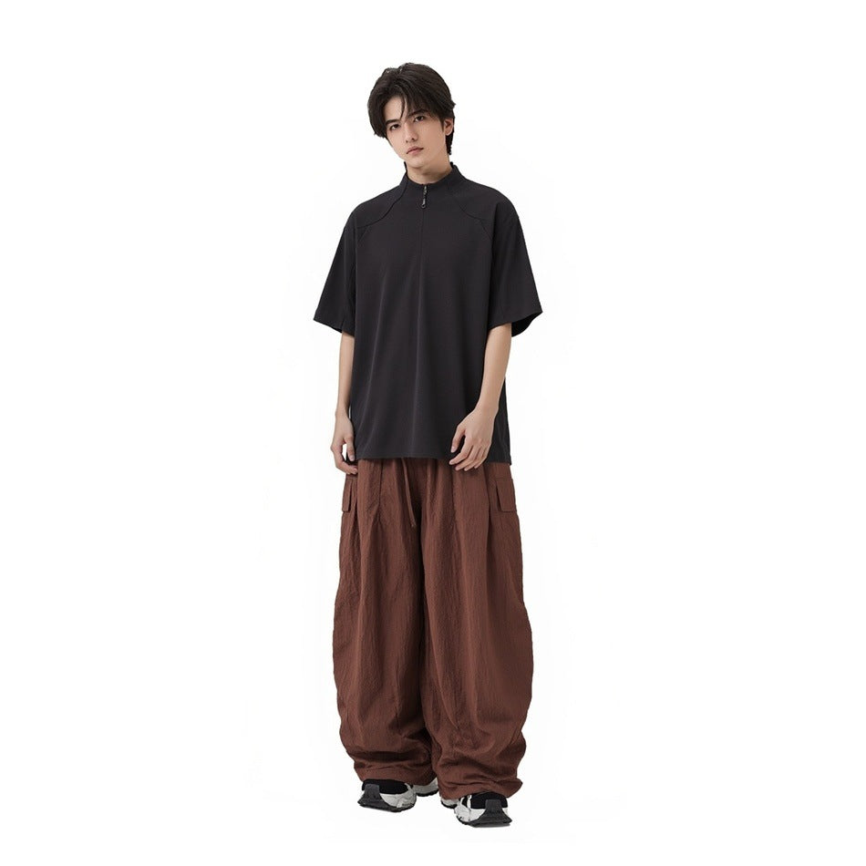 Model wearing an oversized charcoal short-sleeve zip-neck top with loose brown cargo trousers.