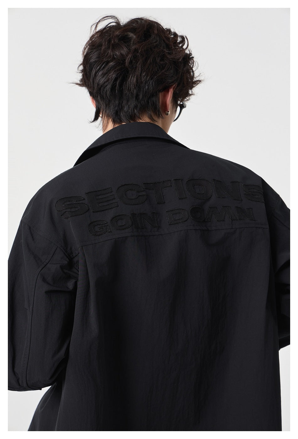 Close-up of black embroidered lettering across the upper back of a black button-up shirt.