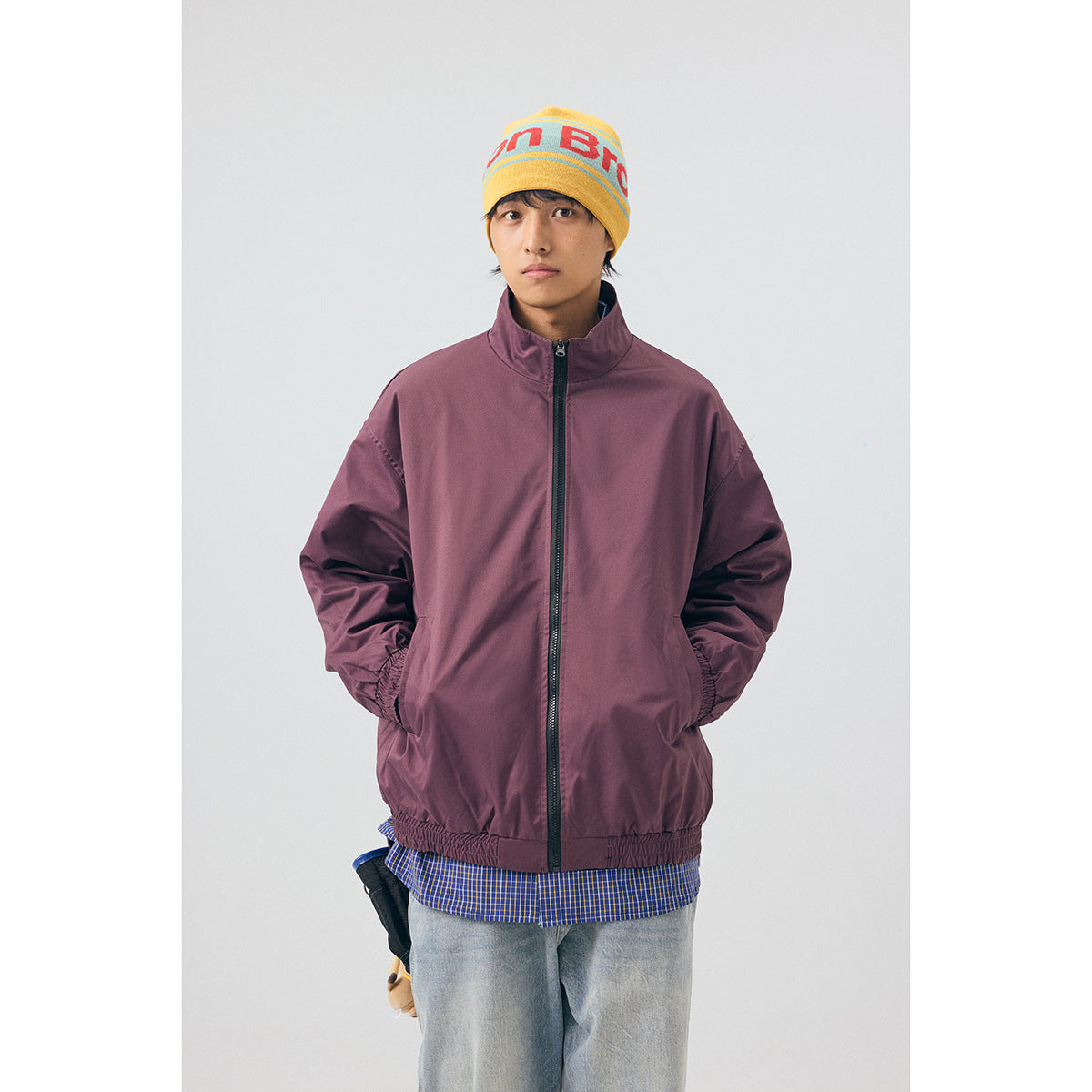 Front view of a model wearing a plum zip-front windbreaker over a blue checked shirt.