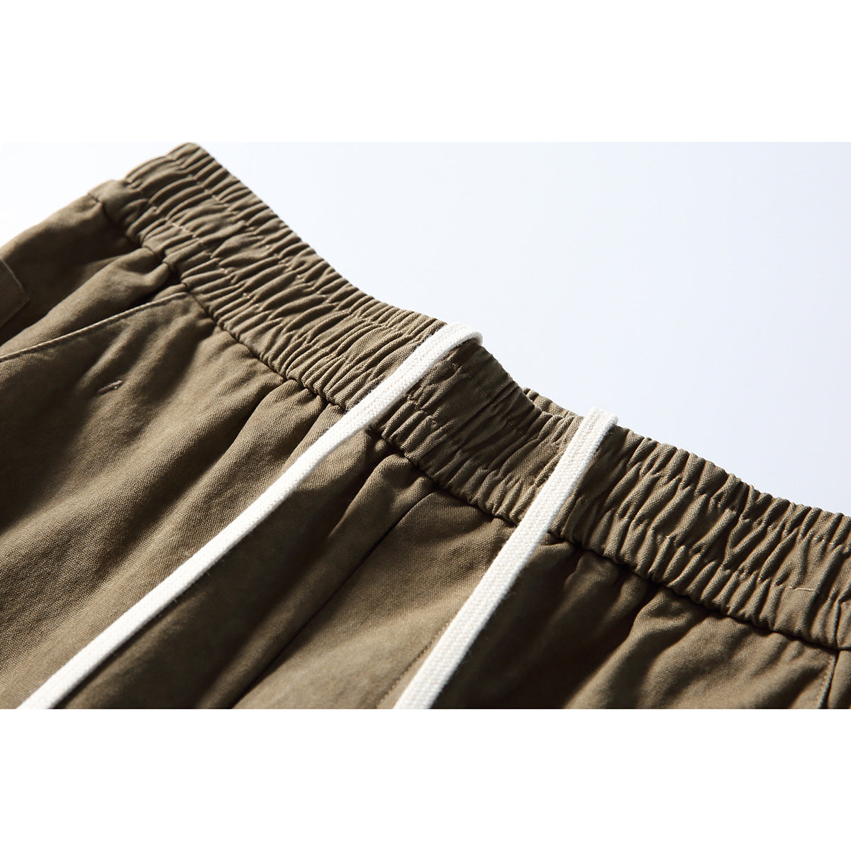 Close-up of olive-brown cargo pants showing a gathered elastic waistband and white drawstrings.