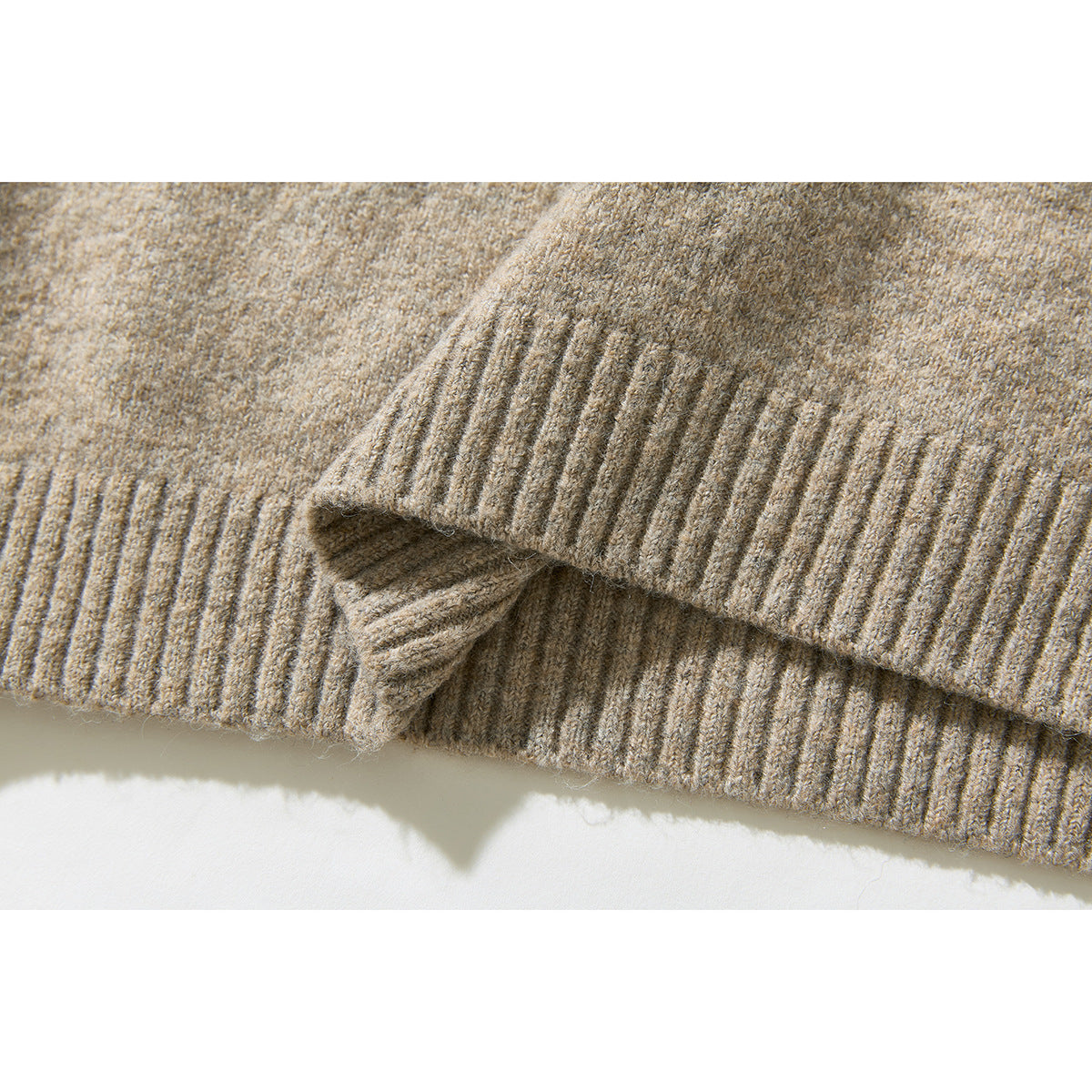 Close-up of the beige heathered sweater's ribbed hem, folded to show its edge.