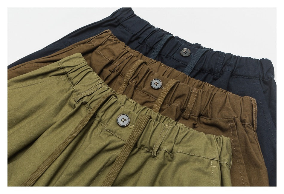 Close-up of three pairs of drawstring pants in olive, brown, and navy, showing elastic waists and buttons.