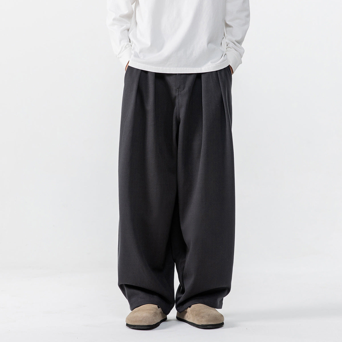 Front view of a person wearing loose, wide-leg charcoal trousers with a white long-sleeve shirt.