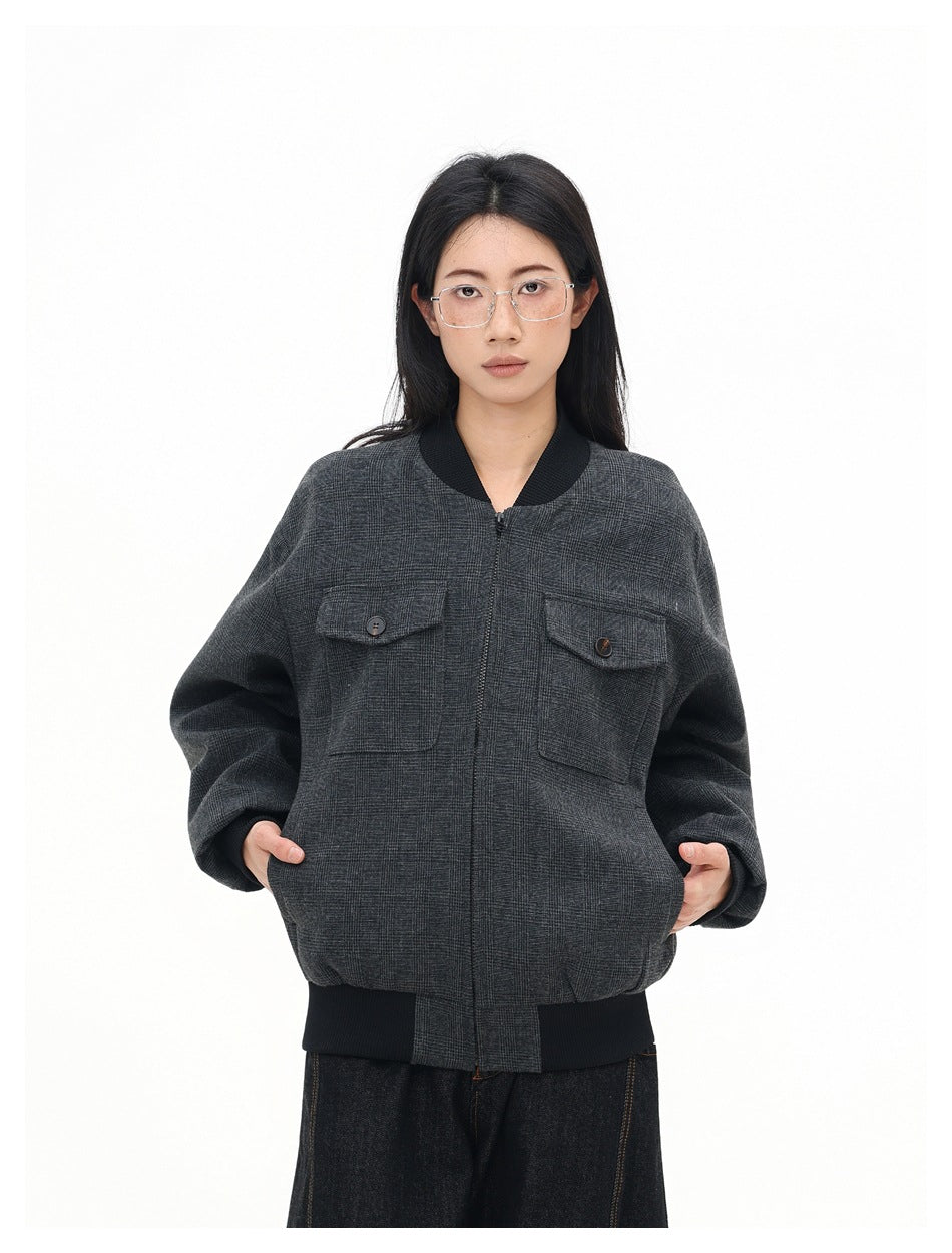Front view of a model wearing a zipped charcoal gray plaid bomber jacket with black ribbed trim and two buttoned chest