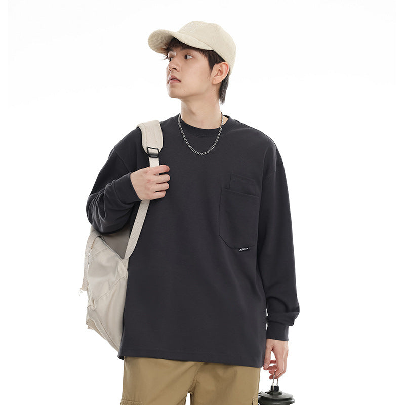 Model wearing a charcoal long-sleeve crewneck shirt with a chest pocket, beige cap, and backpack.