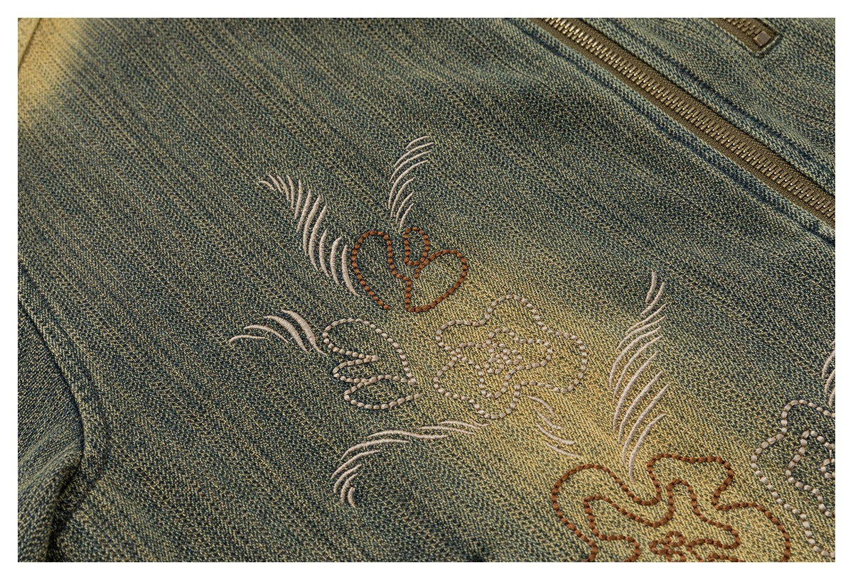 Close-up of floral embroidery in cream and rust on textured olive-gray fabric, with a zipper at the edge.