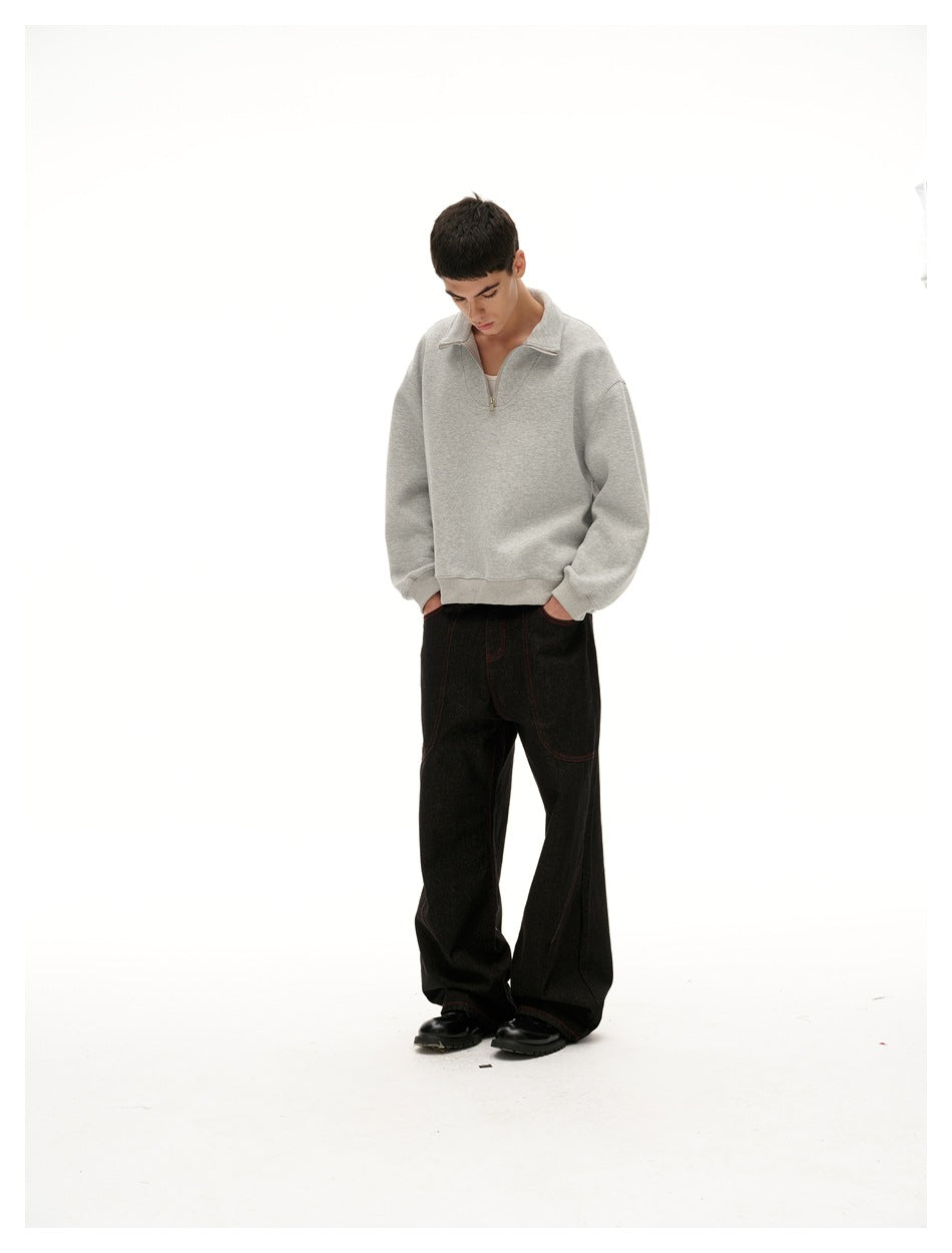 Model looking down while wearing a light gray quarter-zip pullover, black wide-leg pants, and black shoes.