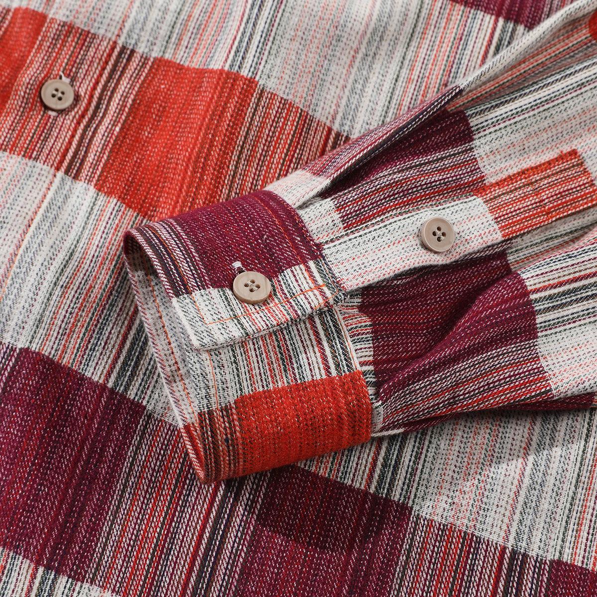 Close-up of a red, burgundy, cream and dark plaid shirt cuff with tan buttons.