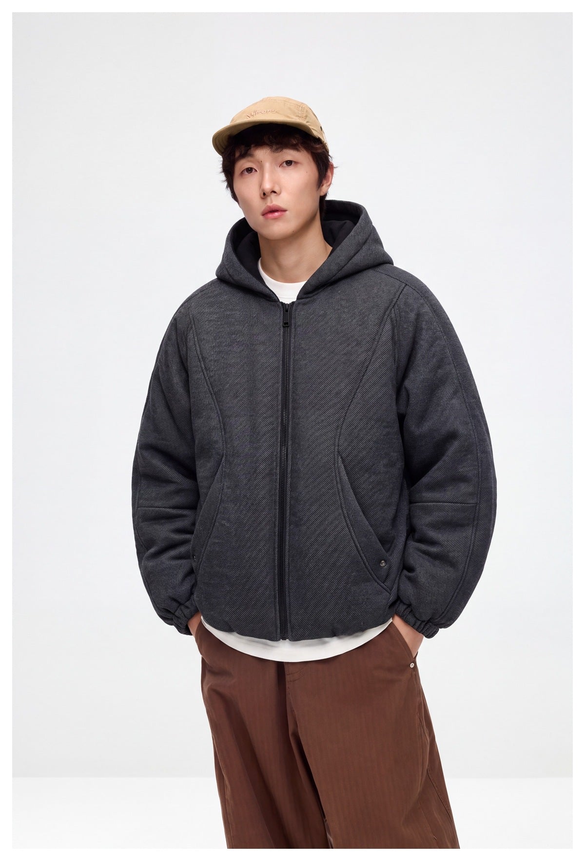 Front view of a model wearing a charcoal hooded zip jacket with curved seams, elastic cuffs, and front pockets.