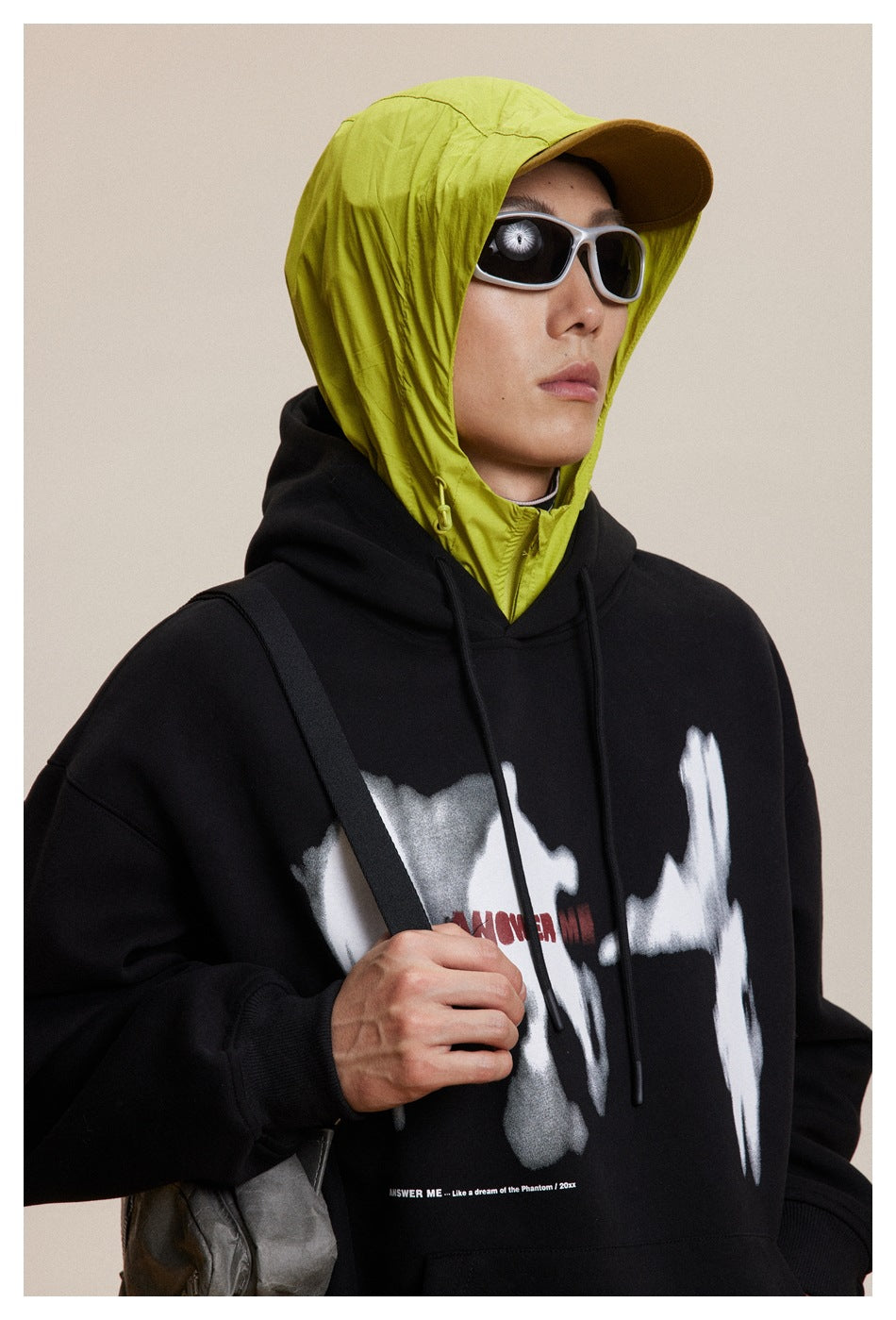 Close view of a black hoodie with a white abstract front graphic, worn over a neon yellow hooded layer.