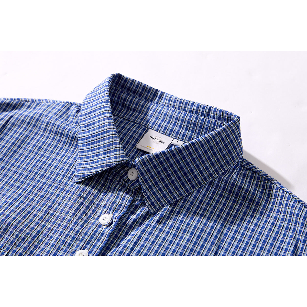 Close-up of a blue plaid shirt collar, white buttons, and inner neck label.