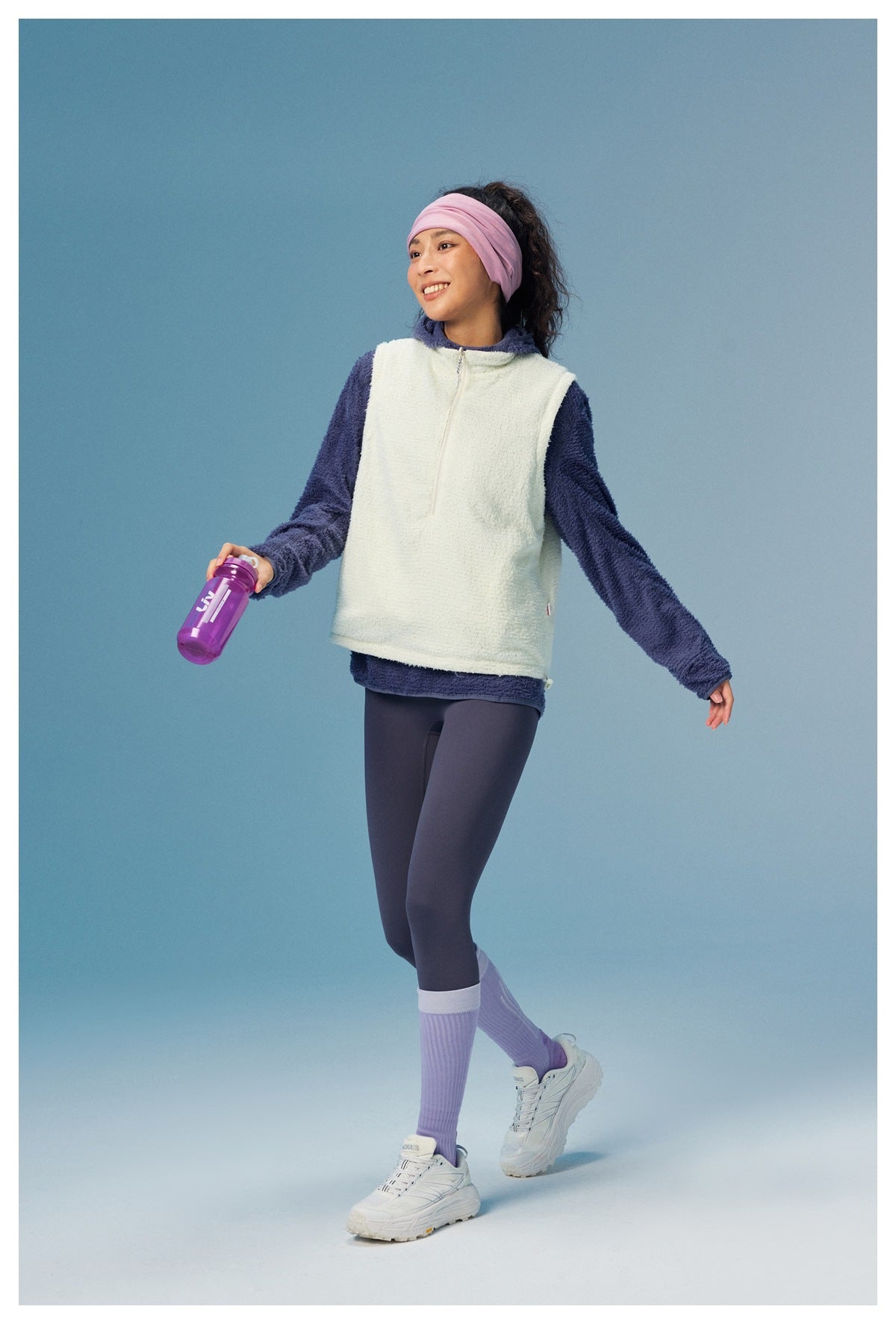 Model wearing an off-white zip vest over a navy fleece top with dark leggings.
