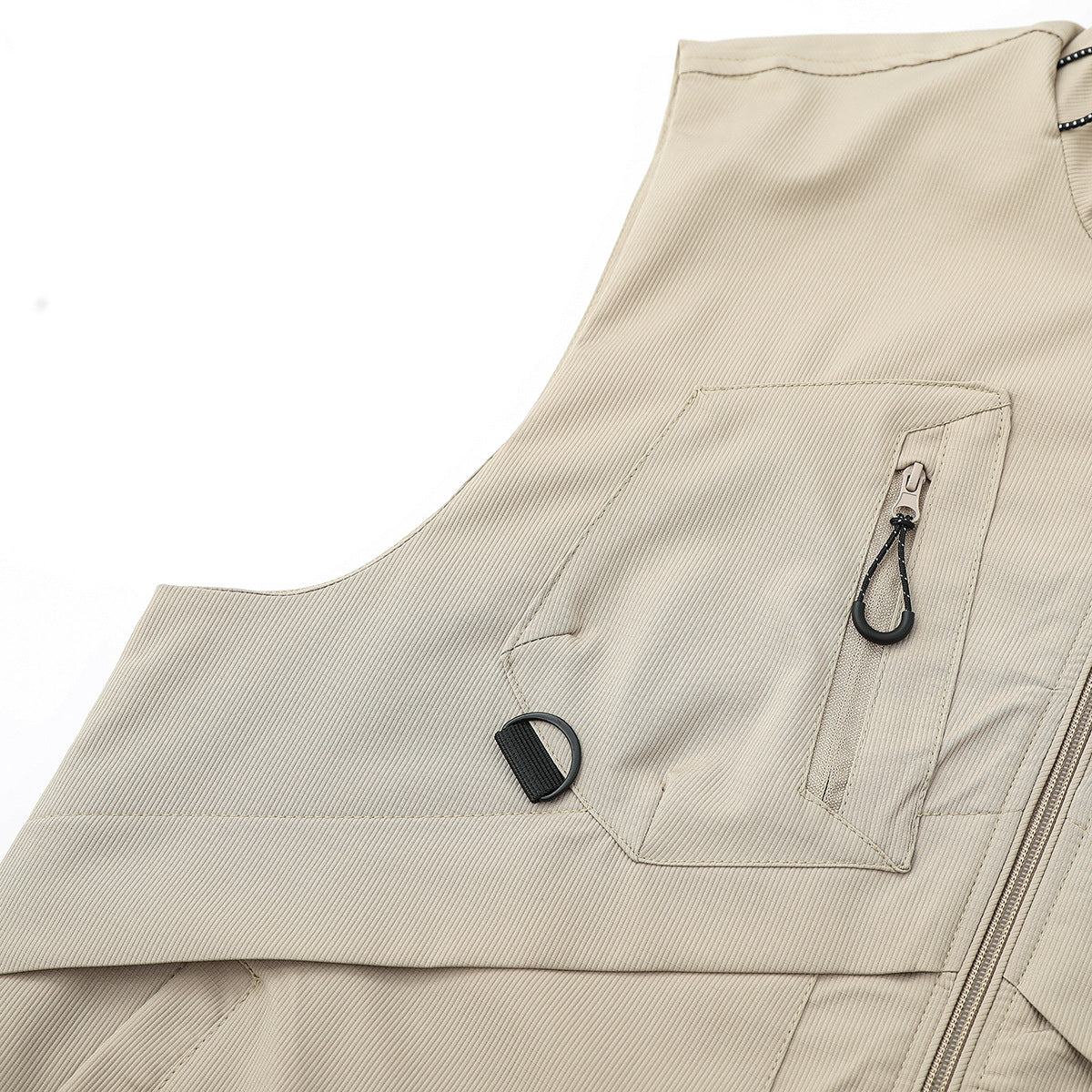 Close-up of a beige vest chest pocket with a vertical zipper, black pull cord, and D-ring.