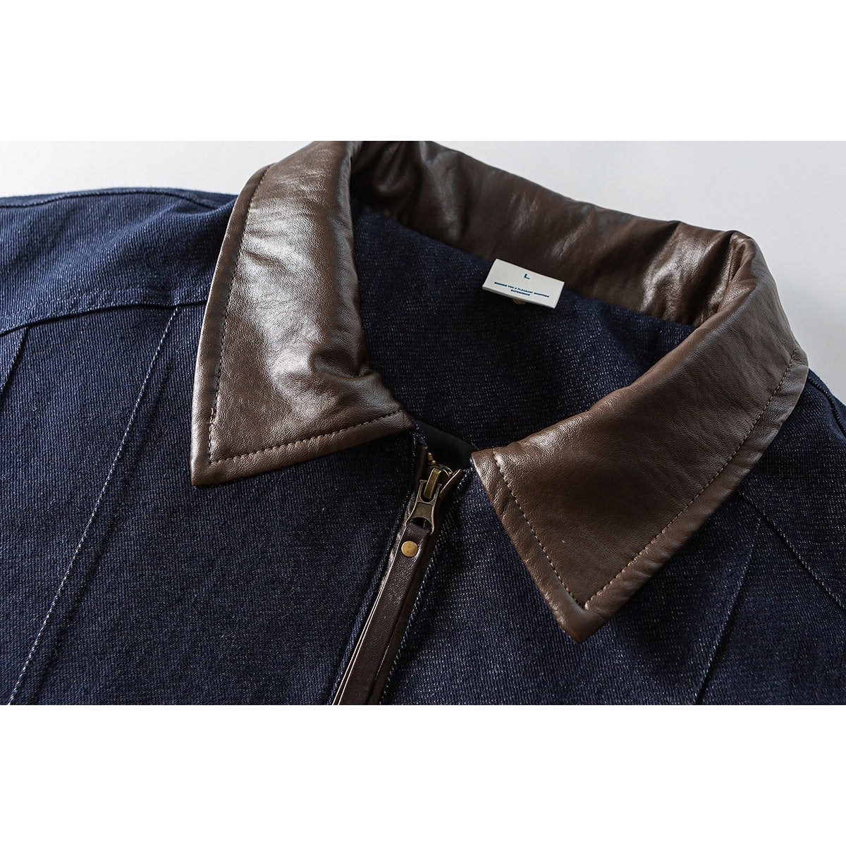 Close-up of a dark indigo jacket with a brown collar, front zipper, and small L size tag.