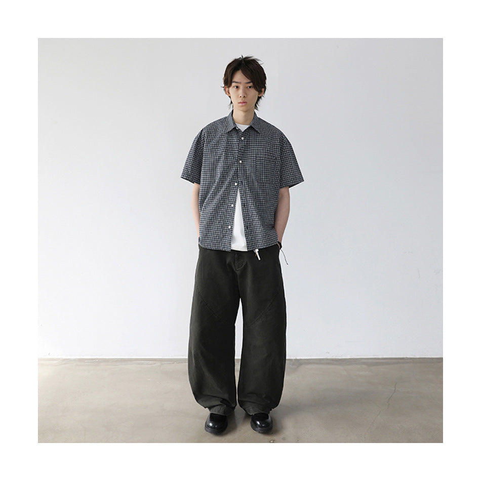 Model wearing plaid short-sleeve shirt open over a white tee with dark green wide-leg pants and black shoes