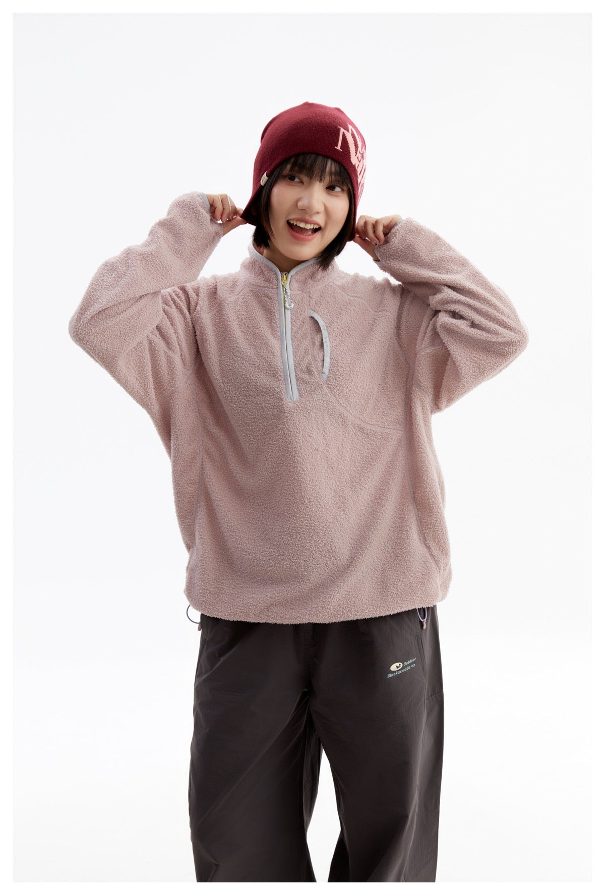 Model wearing a dusty pink fleece pullover with a short zip and curved chest pocket, paired with dark pants.